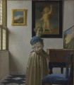Mujer joven de pie ante un barroco virginal de Johannes Vermeer